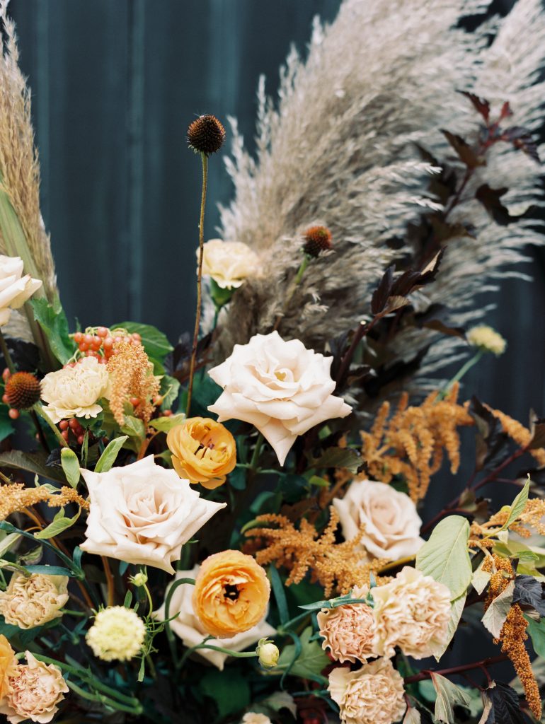 Fall florals embellished with feathers and warm toned flowers offset elegant pink roses in this fall themed bouquet